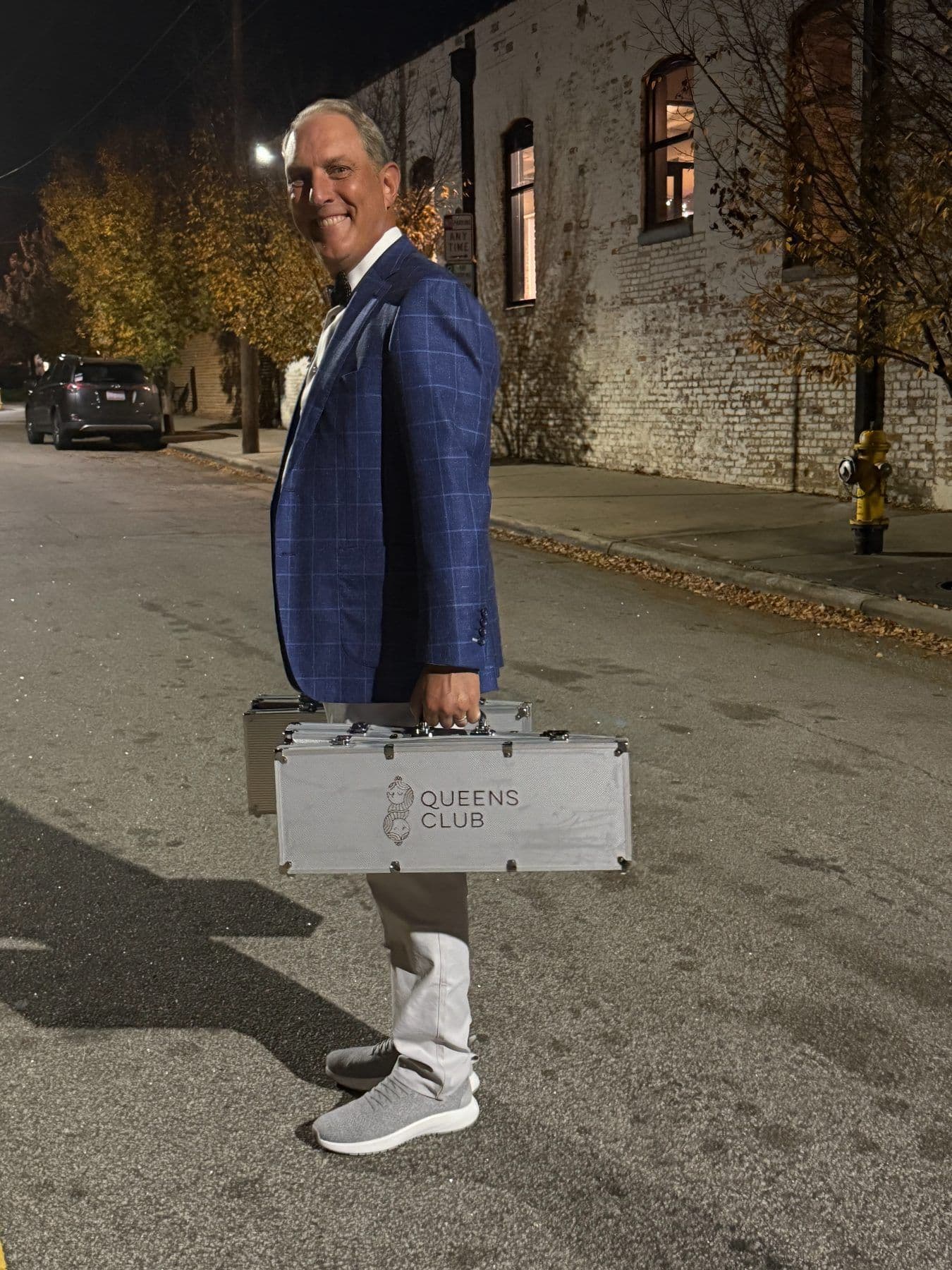 A volunteer carries Queens Club chip cases down a downtown Raleigh street at night